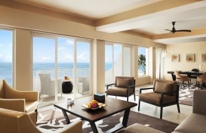 riesige presidenten suite mit hochklassigen wohnbereich lounge und langer glaswand mit ballkon und blick auf das azur blaue meer auf dem tisch steh eine schale mit obst im edlen exotischen luxuriösen und hochklassigen disgner hotel resort vivanta by taj i